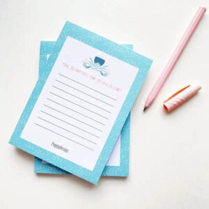 Bilde av to notatblokker oppå hverandre med en rosa penn ved siden av. Notatblokken har blå kant og blomsterdekor