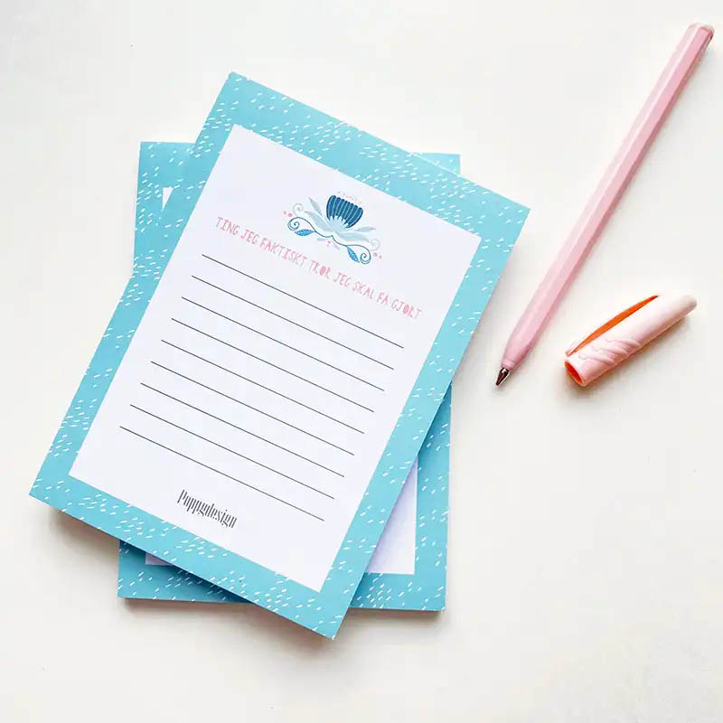 Bilde av to notatblokker oppå hverandre med en rosa penn ved siden av. Notatblokken har blå kant og blomsterdekor