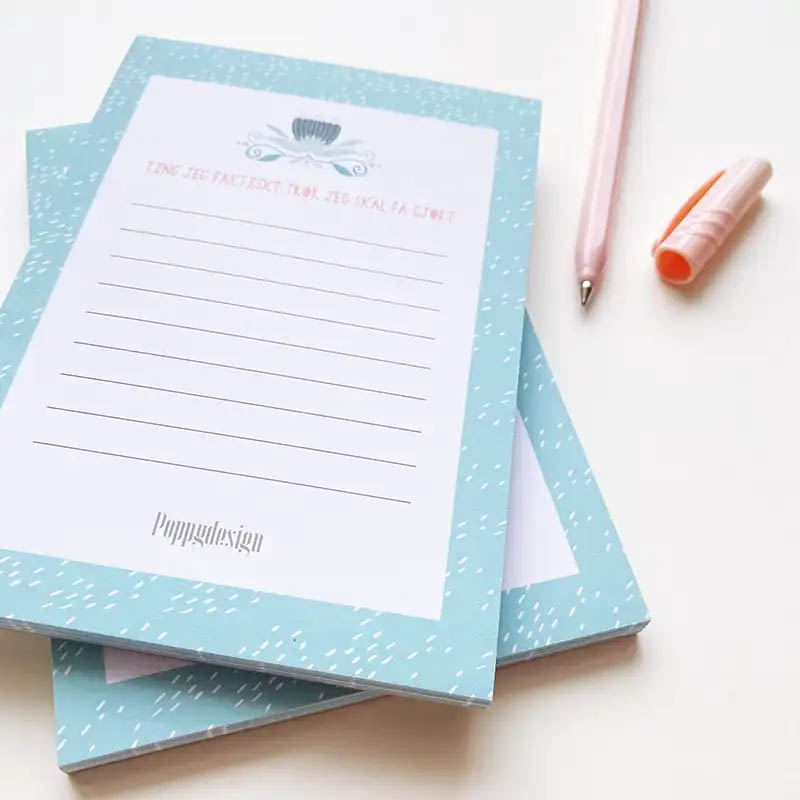 Bilde av to notatblokker oppå hverandre med en rosa penn ved siden av.