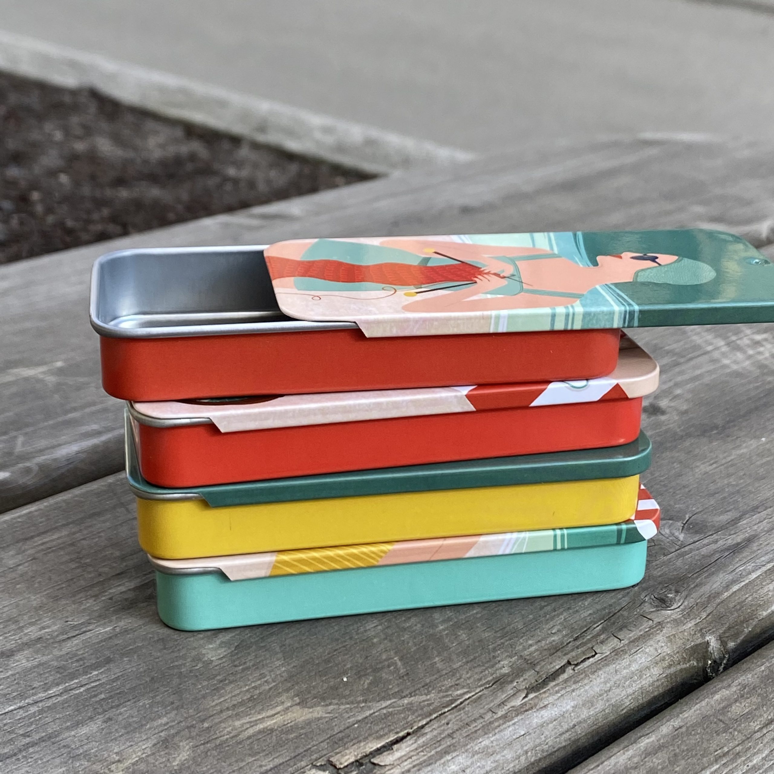 Fire metallbokser med retro motiv i stabel hvor øverste er åpen