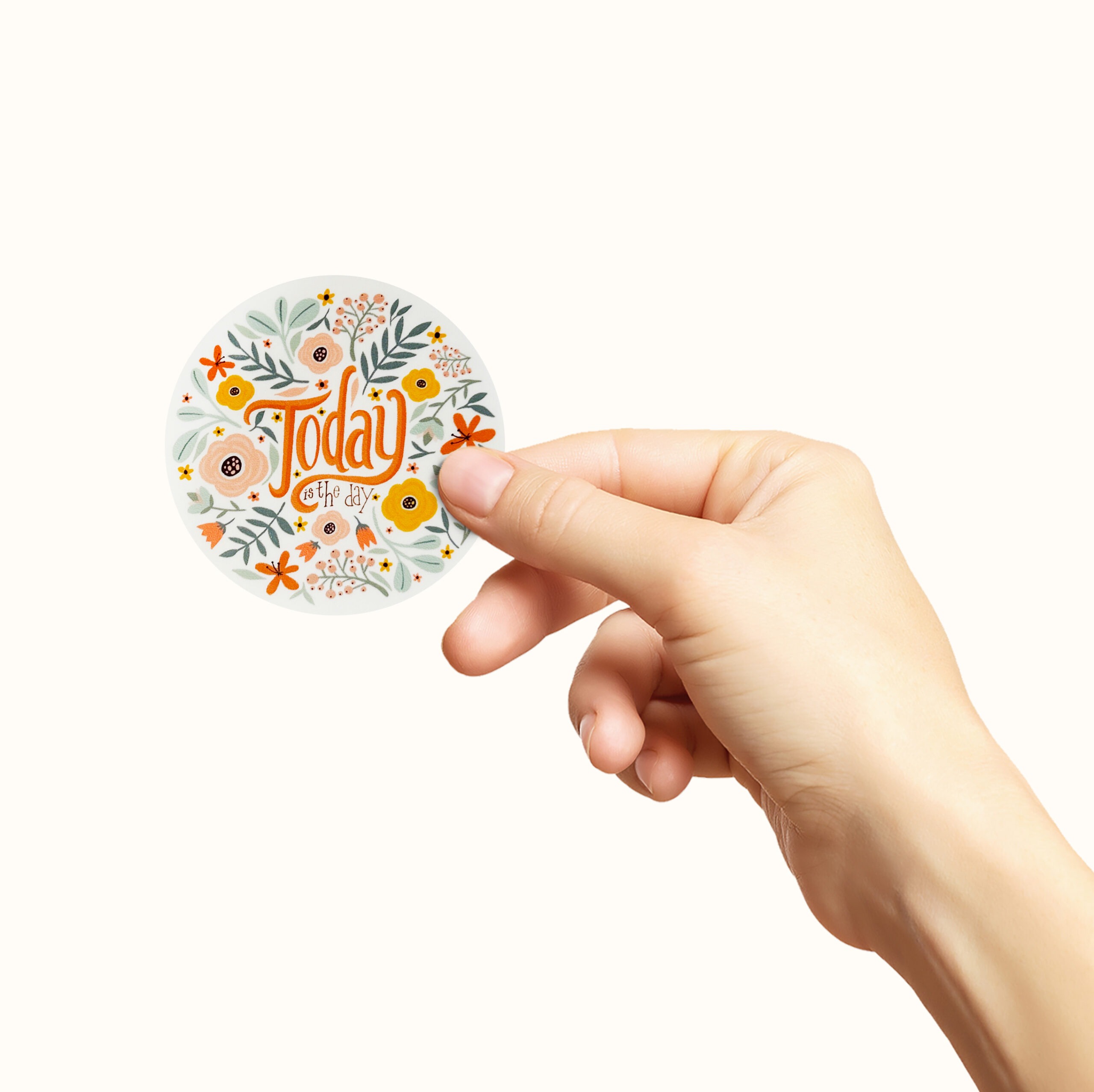 Hånd som holder et firkantet klistremerke med blomster og teksten today is the day