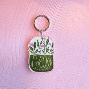 Nøkkelring på rosa bakgrunn med blomster og teksten Grow with the flow